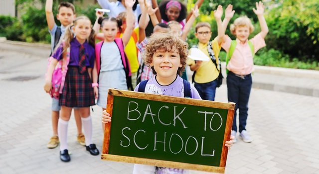 schoolboy with curly hair on the background of a group of children classmates holding a sign with the inscription “back to school.”